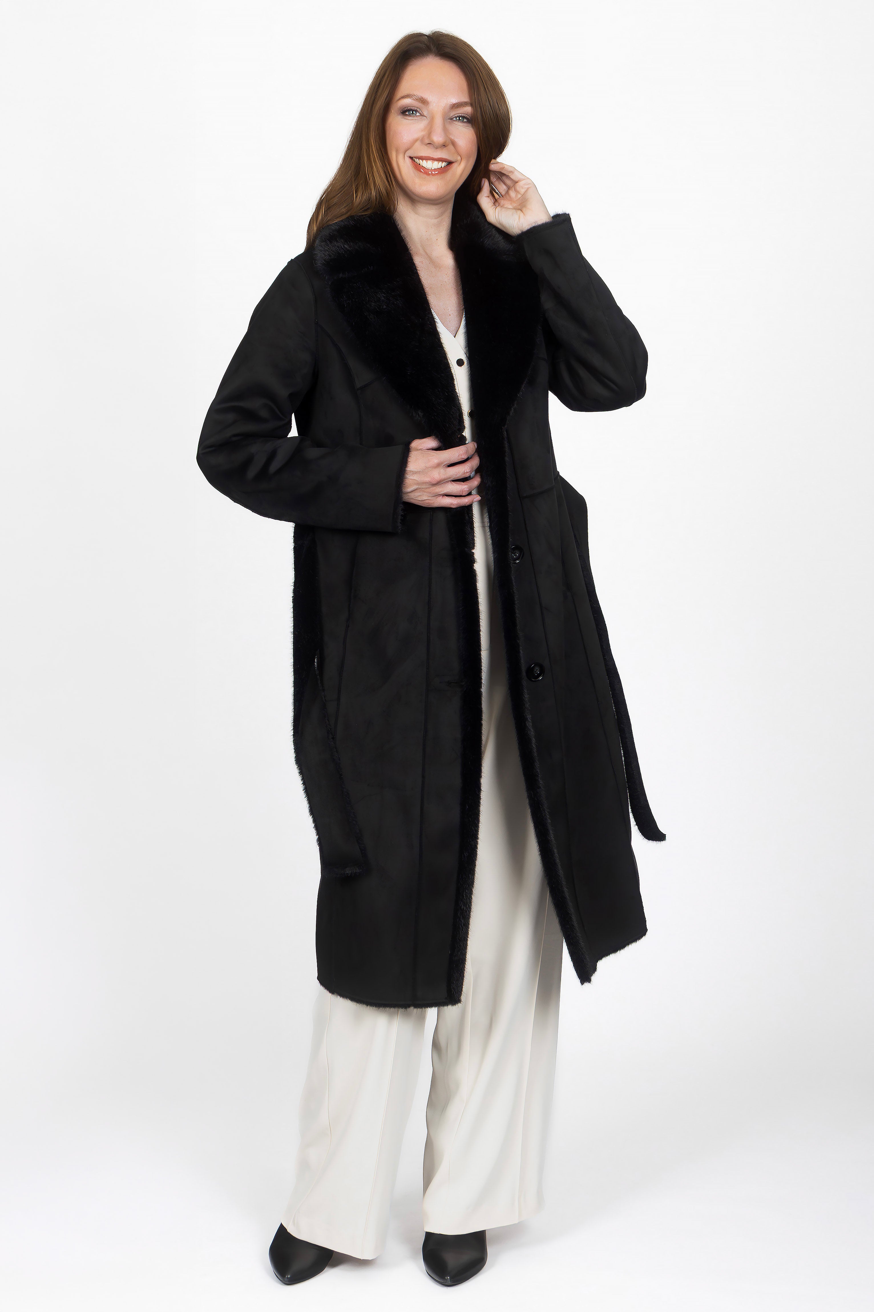 Model trägt den langen Wendemantel in Schwarz mit Lammfell-Optik.