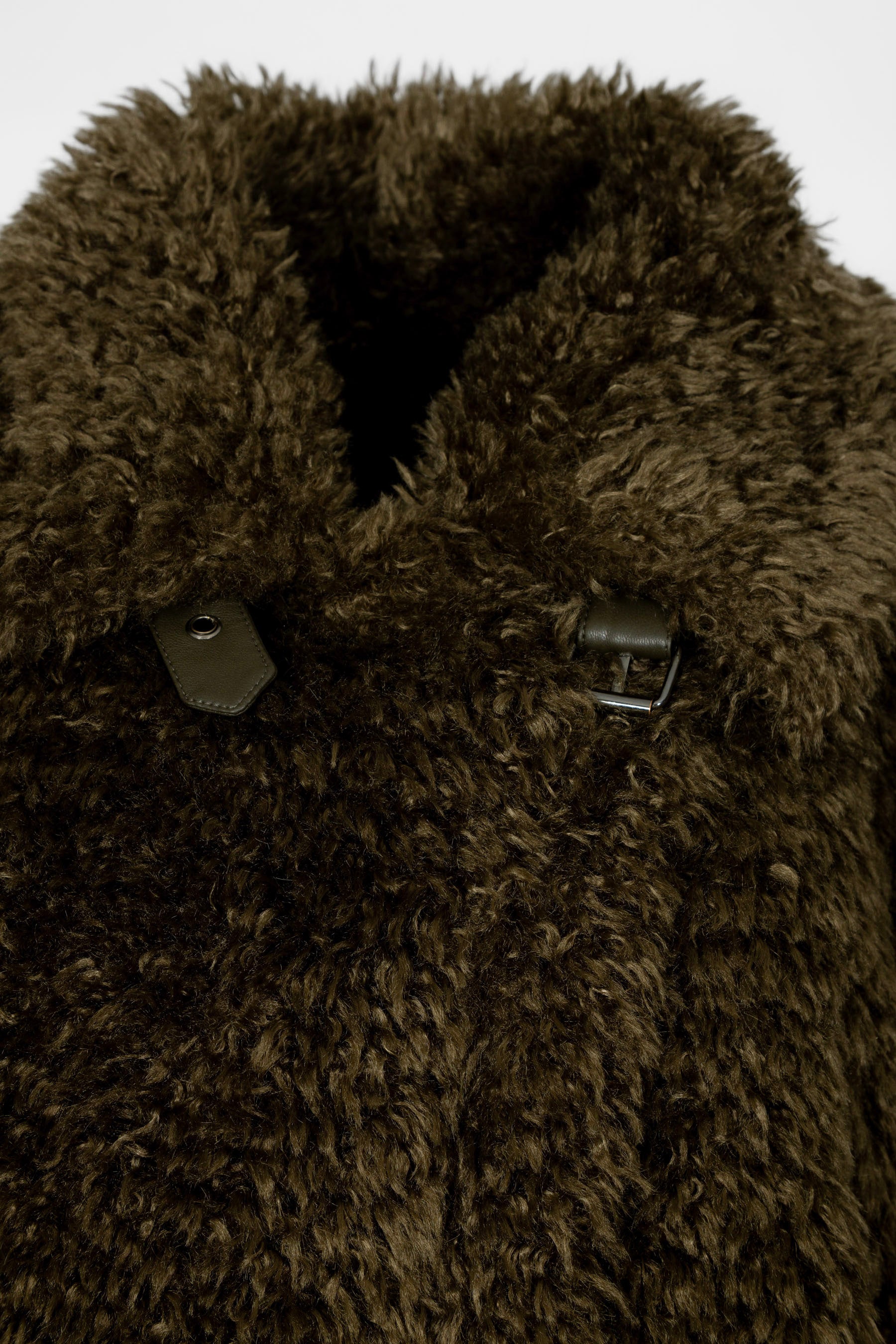 Detailaufnahme vom Damen-Blazermantel in Dunkelgrün aus Teddyfellimitat mit Eco-Leder-Details an Kragen, Taschen und Ärmeln